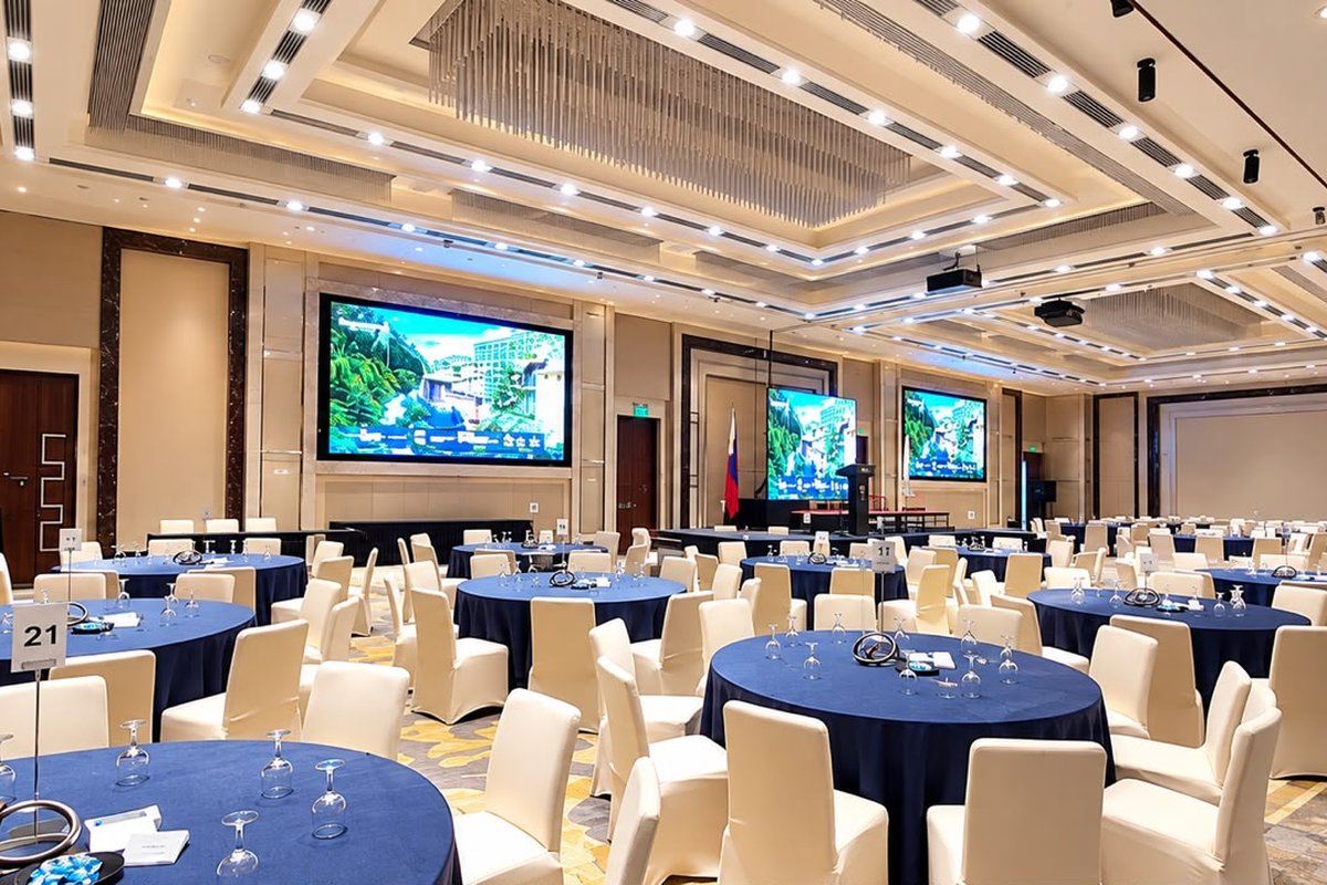 Sheraton Ballroom set for the assembly: round tables in blue linen facing the stage and LED walls